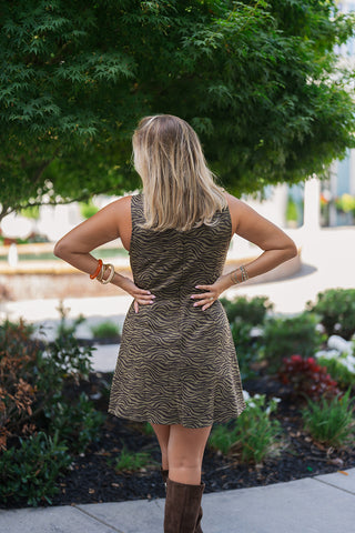 Back view of the Olive Zebra Print Shift Dress showcasing the clean, tailored fit of the sleeveless silhouette. The image highlights the continuous, uninterrupted animal print pattern across the back, featuring a subtle center-back seam and a concealed zipper that provides a smooth, contoured drape. The dress falls to a flattering mid-thigh length, pairing perfectly with the tall brown suede boots for a balanced, sophisticated autumnal aesthetic.