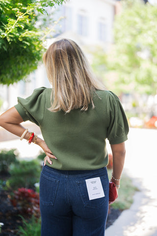 Back views of the Short Puff Sleeve Mock Neck Sweater in both olive green and light beige. The images showcase the continuous, smooth knit fabric and the distinctive volume of the gathered puff sleeves from behind. The slightly cropped, ribbed hem rests cleanly at the waistline of both the dark wash wide-leg denim and the black jeans, highlighting a versatile, flattering, and comfortable fit.