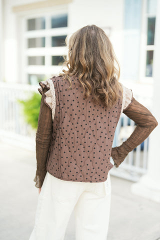 Back view of the chocolate brown quilted polka dot side of the reversible vest, showcasing the diamond quilting stitch pattern and contrast floral lining peeking out along the layered shoulder ruffles.