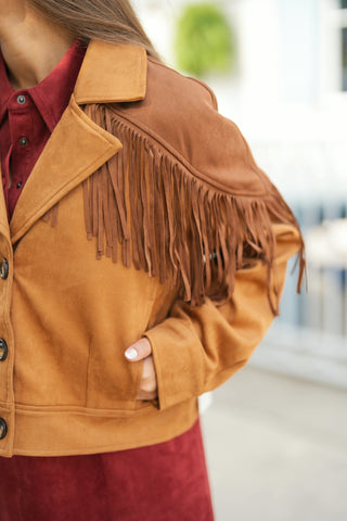 Close-up side view of the camel brown faux-suede fringe jacket highlighting the detailed Western yoke, textured suede material, and dark horn buttons. Showcases the side welt pocket with a hand tucked in, demonstrating the functional fit alongside the layered burgundy shirt underneath.
