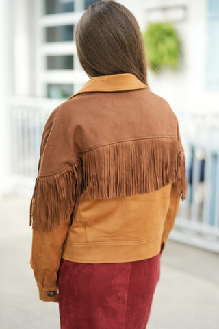 Back view of the camel brown suede fringe jacket showing the distinct two-tone color blocking across the upper back yoke and shoulder panels. Features a dramatic fringe border across the horizontal yoke seam and long sleeves, paired with a fitted burgundy skirt for an elevated Western aesthetic.