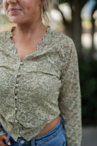 Close-up profile view focusing on the delicate scalloped lace collar, pearlized front buttons, and textured long sleeve on the sage green lace top. Accentuates the sheer floral knit fabric and gold textured hoop earring.
