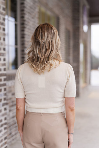 Back view of the Lily Knit Top emphasizing the clean, tailored fit of the soft-touch knit. The image shows the sturdy ribbed waistband and the gentle structure of the puff sleeves, highlighting the top's ability to maintain a polished and secure high-hip fit.