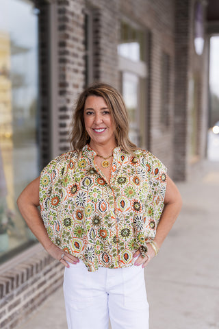 Side view emphasizing the lightweight, breathable woven fabric and the feminine drape of the fluttery short sleeves. The model’s pose highlights the relaxed, slightly boxy fit that allows for a comfortable, airy feel. The intricate globally-inspired pattern stands out against the textured brick background.