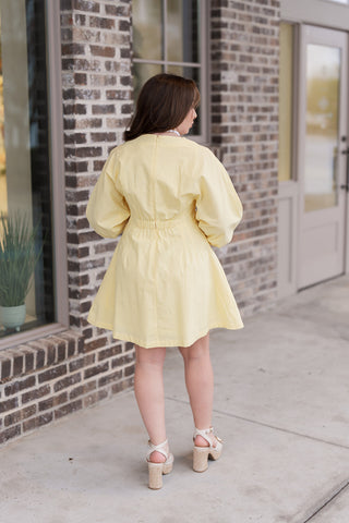 The back view of the Lemon Drop Mini Dress showing the seamless finish provided by the concealed back zipper. The elasticized gathering at the rear waist adds definition to the A-line skirt, while the voluminous puff sleeves maintain their architectural shape from behind.