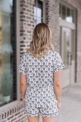 Rear view of the Coquette Dreams Pajama Set showcasing the clean, tailored drape of the short-sleeve top and matching shorts. The continuous black bow motif provides a whimsical yet polished look, emphasizing the breathable and lightweight material ideal for year-round comfort.
