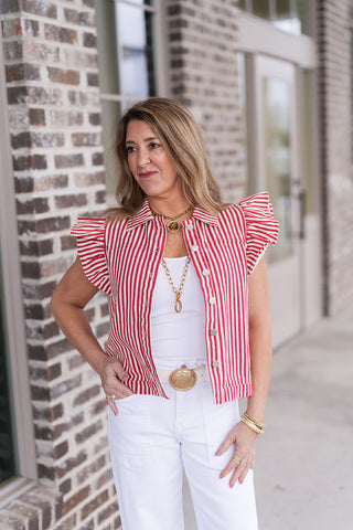 A portrait view of the Regatta Ruffle Vest highlighting the traditional pointed collar and polished metallic button fasteners. The bold red and white striped pattern is complemented by layered gold necklaces, showcasing the vest's architectural ruffle details and structured bodice.