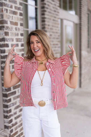 A portrait view of the Regatta Ruffle Vest highlighting the traditional pointed collar and polished metallic button fasteners. The bold red and white striped pattern is complemented by layered gold necklaces, showcasing the vest's architectural ruffle details and structured bodice.