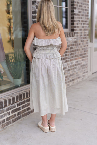 Back view of the Sunlit Stripe Midi Dress, emphasizing the all-over vertical striped pattern and the elegant drape of the voluminous A-line midi skirt. The strapless design continues the smocked bodice for a consistent, secured fit, ideal for effortless summer dressing.