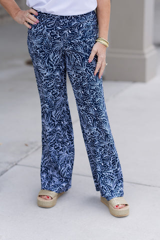 A detailed front view of the Midnight Maritime Pants highlighting the intricate white leaf-inspired pattern against the deep navy base. The tailored front features a smooth, flat-front waistband and is accessorized with stacked gold bracelets and rings, showcasing a high-end "Old Money" aesthetic.