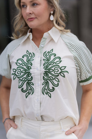 A detailed portrait view highlighting the breathtaking symmetrical emerald green embroidery on the Emerald Estate Button-Down Top. The high-contrast design features a structured pointed collar and 1/2 length puff sleeves with olive green vertical stripes and solid green ribbed cuffs.