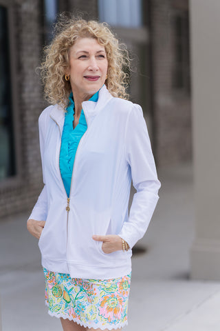 A portrait view of the Ace Athletic Jacket highlighting the sophisticated mock neck collar and the gleaming gold-tone zipper with a custom coin-inspired pull tab. The high-stretch performance fabric is shown layered over a turquoise ruffled polo, emphasizing the gathered puff-sleeve detail that creates a feminine, structured shoulder line.