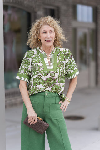 A detailed portrait view of the Palm Pavilion Top highlighting the high-quality woven fabric and sophisticated notched V-neck. The image emphasizes the unique interior striped contrast at the neckline and the structured puff sleeves, accessorized with a layered pearl and gold pendant necklace for a high-end boutique finish.