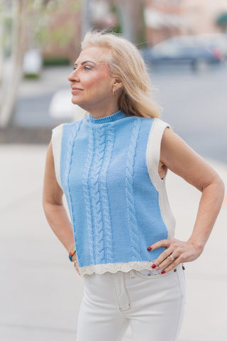 A portrait-style side view highlighting the textural details of the Azure Horizon Vest. The shot emphasizes the traditional heritage cable knit stitching and the delicate, white scalloped accent hem that provides a whimsical boutique finish. The sleeveless, tailored silhouette hits at the natural waistline, showcasing the high-quality, non-sheer construction of the garment.