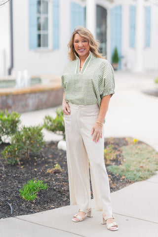 Model posing in the Matcha Garden Gingham Top tucked into high-waisted, wide-leg beige linen trousers with front patch pockets. This view showcases the top's relaxed yet polished drape and its non-sheer, unlined construction, perfect for a sophisticated, airy spring look.