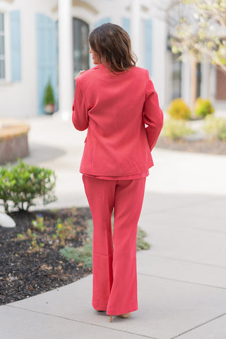 The back view of the Watermelon Sugar Blazer showcasing its modern, contoured tailoring and clean silhouette. The rich, saturated coral fabric offers a smooth, wrinkle-resistant drape, with a central back seam and structured shoulders that provide a sharp, professional frame. Paired with the matching coral trousers, the look emphasizes a cohesive, high-end "desk-to-dinner" aesthetic.
