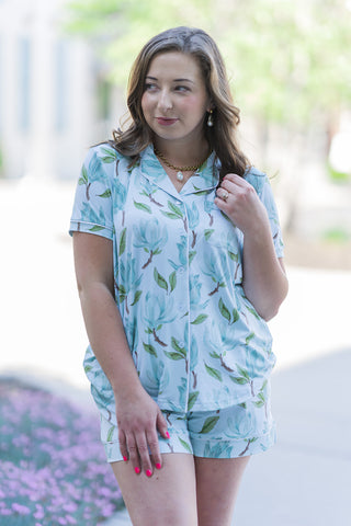 A detailed portrait view of the Magnolia Garden Sleep Shirt highlighting the sophisticated notched collar, white piping along the front placket, and a functional chest pocket. The lightweight, breathable fabric showcases the high-definition magnolia blossom print. The woman is styled with a gold pearl necklace, demonstrating how this elevated sleepwear transitions effortlessly from bed to morning coffee.
