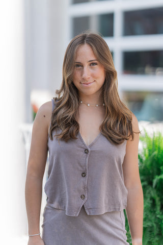 A medium close-up view highlighting the details of the Z Supply Perfectly Taupe Noelle Top. The shot showcases the soft texture of the 100% cotton jersey fabric and its unique, vintage-inspired mineral wash finish. Key design elements are visible, including the clean-edged V-neckline, three dark contrasting buttons, and a structured, pointed waistcoat-style hemline.