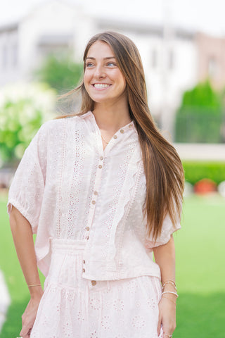 A medium front shot of a smiling model showcasing the light pink Rosewater Romance Lace Blouse. The image focuses on the classic spread collar, functional front placket with contrasting neutral buttons, and the vertical lace panels with scalloped appliqué trims running down the bodice.