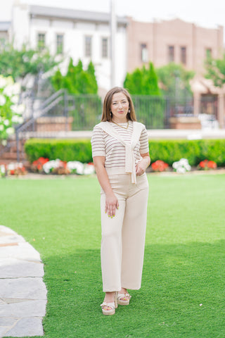 Full-length front view of a model posing in the ecru Parisian Port Stripe Top. The short-sleeve knit top is tucked into high-waisted, cream structured knit pants and styled with neutral woven block-heel platform sandals for a chic, monochromatic resort aesthetic.