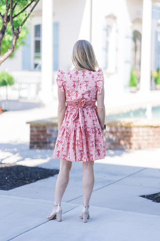 Back view of the Peachy Keen Ruffle Mini Dress demonstrating the effortless, defining fit of the back elastic waistband, which is finished with a charming fabric tie detail. The image captures the breezy flutter sleeves and the subtle tier detail along the mini-length hemline. The fully lined, lightweight dress provides complete coverage while maintaining a fresh, feminine energy.