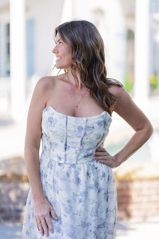 A portrait view of the Coastal Cloud Slit Dress highlighting the intricately engineered bodice. The tailored sweetheart neckline and faux-corset waist featuring vertical boning details are clearly visible, perfectly defining the silhouette. The sheer chiffon overlay highlights a dreamy watercolor botanical floral pattern over a creamy background, simply accessorized with a delicate cross pendant necklace.