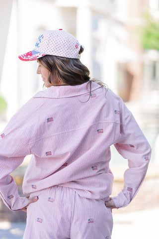 Back view of the Stars & Stripes Seersucker Buttondown displaying the oversized, boyfriend-style fit and clean back yoke detailing. This angle emphasizes the continuous red-and-white pinstripe seersucker fabric and the subtle, scattered placement of the embroidered American flags, shown paired seamlessly with the matching lightweight shorts.
