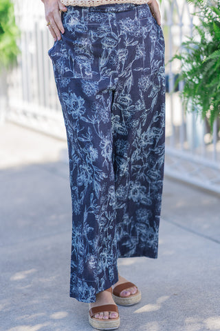 Pants. The image highlights the clean, flat-front high-rise waist and the distinctive, oversized square patch pockets positioned flat at the hips. The lightweight, breathable woven fabric drapes beautifully into a wide-leg cut, showcasing the elegant, highly detailed navy blue and white botanical print.