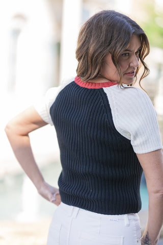 Back view of the Americana Heritage Ribbed Knit top, displaying the clean, uninterrupted texture of the deep navy vertical ribbing that naturally hugs the silhouette. This angle highlights the seamless integration of the white raglan shoulders and the bright red ribbed crew neckline from behind, styled effortlessly with white denim.