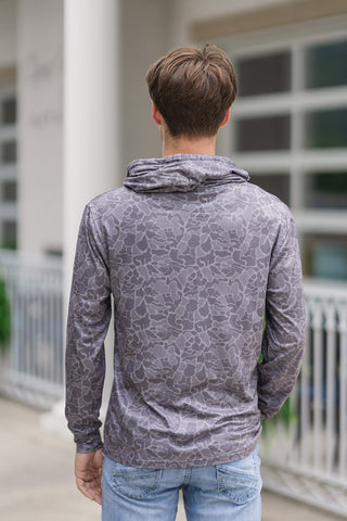 Back view from the waist up of a young man wearing the Shadow Camo Performance Hoodie, highlighting the continuous pattern flow across the reverse side. The lightweight, wrinkle-resistant fabric drapes smoothly over the back and arms, emphasizing a flexible athletic fit. The built-in hood is kept relaxed at the base of the neck, and the look is completed with light-wash blue jeans.