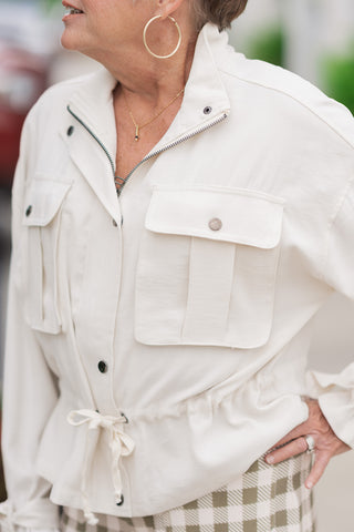 A detailed close-up shot focusing on the artisanal and utilitarian elements of the Canyon Clay Cargo Jacket bodice. The image highlights the prominent, pleated cargo chest pockets with metallic snap-flap closures, the dual zipper and snap-button placket, and the gathered tunnel casing for the front-tying fabric drawstring. The model is accessorized with large gold hoop earrings and a delicate gold pendant necklace.