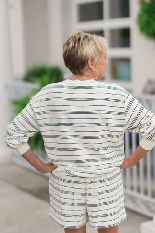 Back view from the waist up of a woman wearing the Z Supply Stand Out Sweatshirt, highlighting the clean, continuous alignment of the horizontal black stripes across the reverse side. The dropped shoulder seams and slouchy drape flow seamlessly down to a wide ribbed hemline, demonstrating a structured yet highly comfortable casual fit over the matching striped shorts.