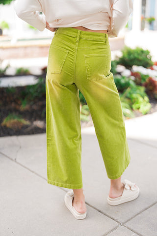 Back view of the Matcha Latte Corduroy Pants demonstrating the flattering high-rise fit and clean rear design. The image showcases the two functional back patch pockets and the structured, comfortable fit across the hips, leading down to a wide-leg hemline paired with off-white bow platform slides.