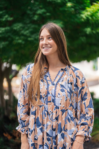 A portrait view of the Seaside Mosaic Midi Dress detailing the split v-neckline trimmed with intricate navy crochet-style lace embroidery. The close-up showcases the gathered empire seam, the voluminous 3/4-length sleeves with elastic ruffled cuffs, and the rich texture of the blue and tan abstract mosaic print.