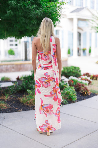 Back view of the Hawaiian Hibiscus One-Shoulder Maxi Dress showcasing the elegant silhouette and fluid movement of the maxi skirt from behind. This angle highlights the built-in shoulder drape panel that falls gracefully down the side of the dress for a dramatic, cape-like effect, while the vibrant hibiscus motifs align beautifully across the smooth, unlined fabric.