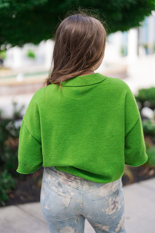Back view of the Metropolitan Mod Top highlighting its comfortable, slightly cropped boxy silhouette and clean unlined drape. The vivid chartreuse-lime green lightweight knit top features dropped shoulders and a thick, defined ribbed trim wrapping around the neckline and bottom hem, sitting cleanly over floral-patterned denim.