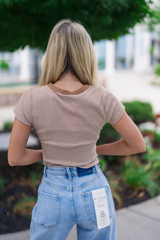 Back view of the Mixtape Memories Striped Tee showcasing the clean, continuous flow of the fine chocolate brown and white horizontal micro-stripes across the shoulders and back. This view highlights the contrast ringer neckline and shows how the body-contouring straight hemline rests perfectly against the waistband of high-rise light-blue denim jeans.