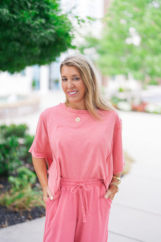 A medium portrait shot of the Raspberry Sunrise Top highlighting its relaxed boxy fit and comfortable wide boat neck. The close-up showcases the beautiful texture irregularities from the specialty mineral wash process, along with striking vertical contrast seam details extending down the front of the body and across the short dropped-shoulder sleeves.