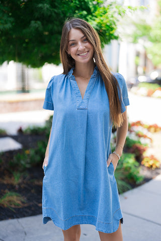 A detailed portrait view of the Sweet Magnolia Chambray Dress highlighting the structured ruffled band collar framing the neck. The soft-wash, lightweight chambray fabric gives the appearance of denim with a relaxed drape, beautifully accented by a crisp split V-neckline and delicate gathered shoulders on the short sleeves.