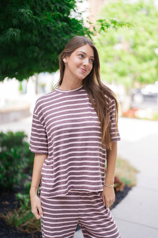 A medium portrait shot highlighting the casual drape and premium texture of the Wildberry Boardwalk Tee. The close-up emphasizes the clean, standard ribbed crew neck and loose short sleeves with dropped shoulders. The lightweight brushed knit blend offers a soft visual texture, accessorized subtly with gold bracelets and simple rings.