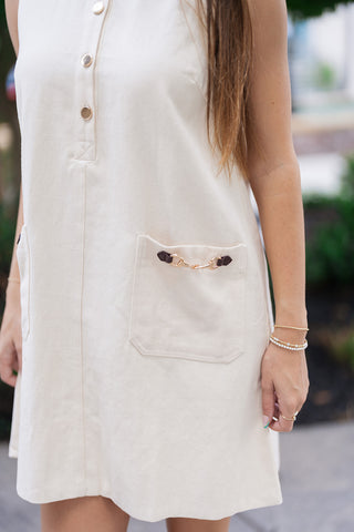 A detailed close-up shot focusing on the high-end tailoring elements of the Upper East Side Pocket Dress. The image highlights the functional front patch pockets adorned with dark brown faux-leather tabs and equestrian-inspired gold buckle hardware, alongside gleaming gold-tone buttons lining the partial front placket.