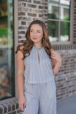 A portrait view of the Z Supply Sloane Eclipse Striped Top highlighting its clean crew neckline and breathable, premium yarn-dyed texture. The vertical cream and navy blue stripes offer a timeless maritime look. The top is accessorized with a bold gold statement necklace and delicate bracelets, showcasing an effortless, everyday boutique style.