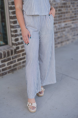 A close-up view focusing on the front and side profile of the Z Supply Scout Eclipse Striped Pants. The image showcases the flattering high-rise waistline, the functional side slash pockets with the model's hand tucked inside, and the billowy, wide-leg silhouette. The detailed, premium texture of the lightweight yarn-dyed stretch knit fabric is highly visible, paired with open-toe platform sandals featuring a gold buckle.
