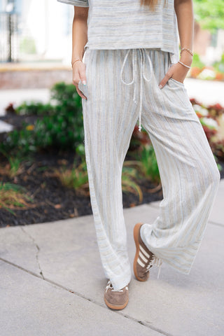 A close-up view focusing on the matching trousers of the Ocean Breeze Lounge Set. The image highlights the cozy, flexible elasticated waistband with an adjustable cream drawstring tie. The lightweight textured knit fabric falls into a relaxed, wide-leg silhouette with vertical striping that elongates the frame. The model has her hands placed casually inside the functional side pockets.