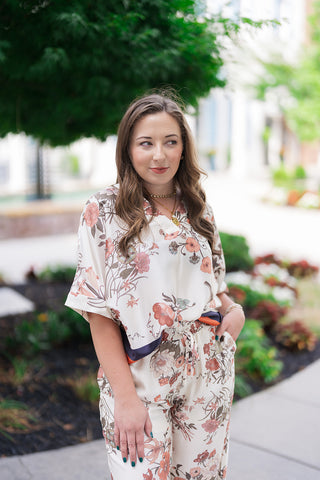 A portrait view of the Venice Vineyard Blouse highlighting its sophisticated, clean-cut open V-neckline and billowy dolman-style short sleeves with distinct folded cuff details. The close-up emphasizes the high-quality, un-clingy drape of the premium fabric and the intricate details of the terracotta, dusty rose, and muted sage green floral blooms against the soft cream base.