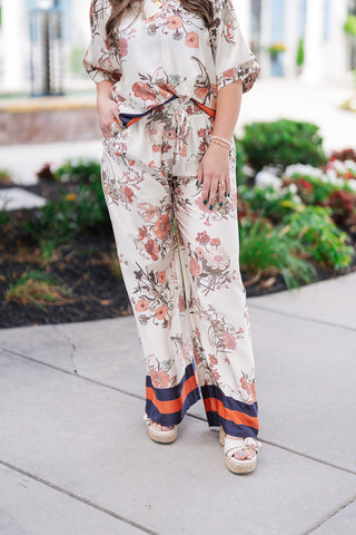 A mid-length view highlighting the structural and functional details of the Venice Vineyard Pants. The image showcases the high-rise elasticated waistband with an adjustable drawstring and a model's hand resting in the hidden side pocket. The flowing wide legs drape beautifully toward the hem, showcasing the bold, graphic navy blue and terracotta orange contrast stripe border.