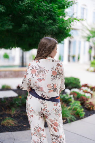 Back view of the Venice Vineyard Blouse highlighting the fluid, unrestrictive drape across the shoulders and back. This view showcases how the organic botanical floral pattern seamlessly transitions down to the straight hemline, which is finished with a striking navy blue and terracotta orange graphic contrast border print resting over the matching high-waisted trousers.