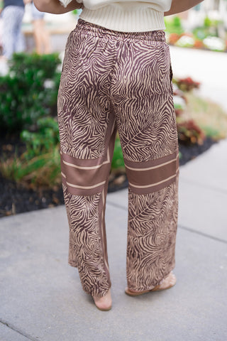 Back view focusing on the Java Jungle Wide-Leg Pants to illustrate the fluid drape and premium alignment of the fabric. The continuous abstract animal print flows smoothly over the body, while the geometric horizontal border panels weight the lower legs to highlight the billowy, non-sheer wide-leg silhouette from behind.