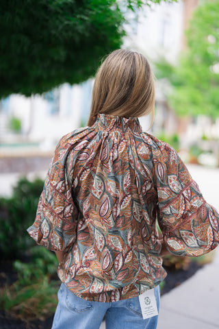 Back view of the Canyon Spice Botanical Top illustrating the continuous flow of the terracotta, sage green, and mustard yellow botanical print. The high smocked collar creates beautiful gathers that drape loosely down the back bodice, while the structural volume of the puff sleeves remains perfectly intact over the waistband of her light-wash denim.