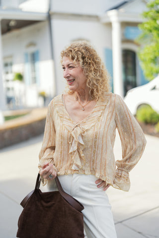 Three-quarter portrait of a woman wearing the semi-sheer yellow striped romantic blouse, highlighting the open V-neckline framed by soft cascading ruffles, a front tie detail, and airy long blouson sleeves with smocked ruffle wrists.
